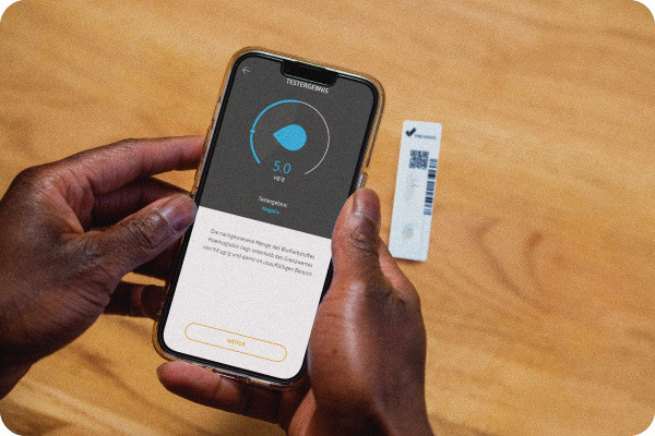 Person scannt zuhause Testkassette zur Darmkrebsvorsorge mit iPhone und erhaelt Zahlenwert.
